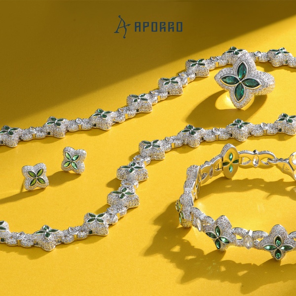 A high-end 1:1 ratio studio shot of a clover-themed jewelry set featuring a necklace, bracelet, ring, and earrings against a vibrant yellow background.